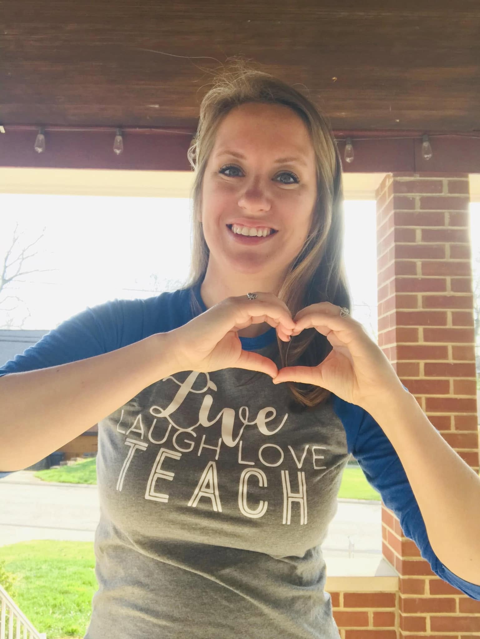 Carrie Williams making a heart shape with her hands, wearing a shirt that reads Live Laugh Love Teach